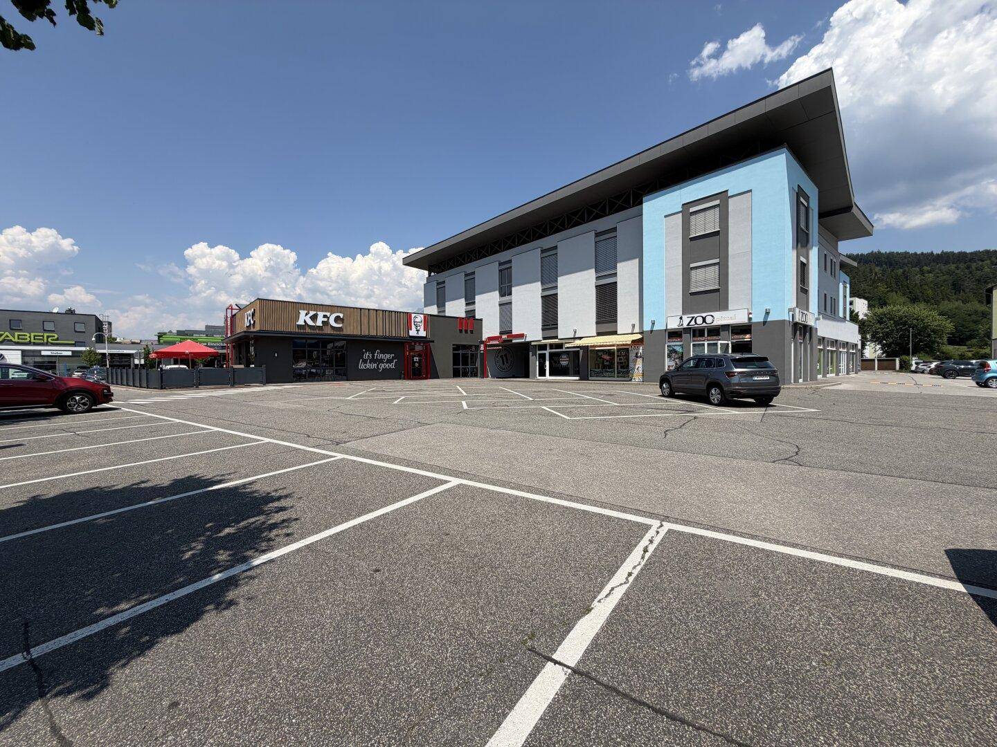 Gesamtansicht des modernen Gebäudekomplexes mit Fast-Food-Restaurant und weitläufigen Parkflächen.