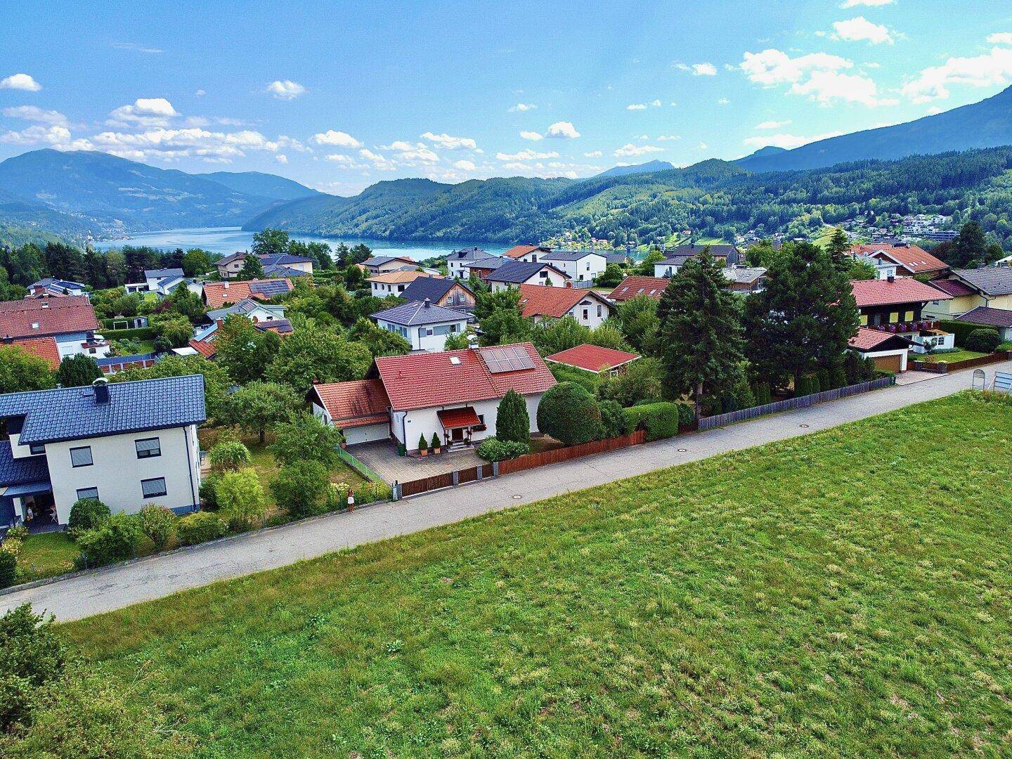 Panoramablick auf eine Wohnsiedlung mit See und Bergen, umgeben von üppiger Natur.