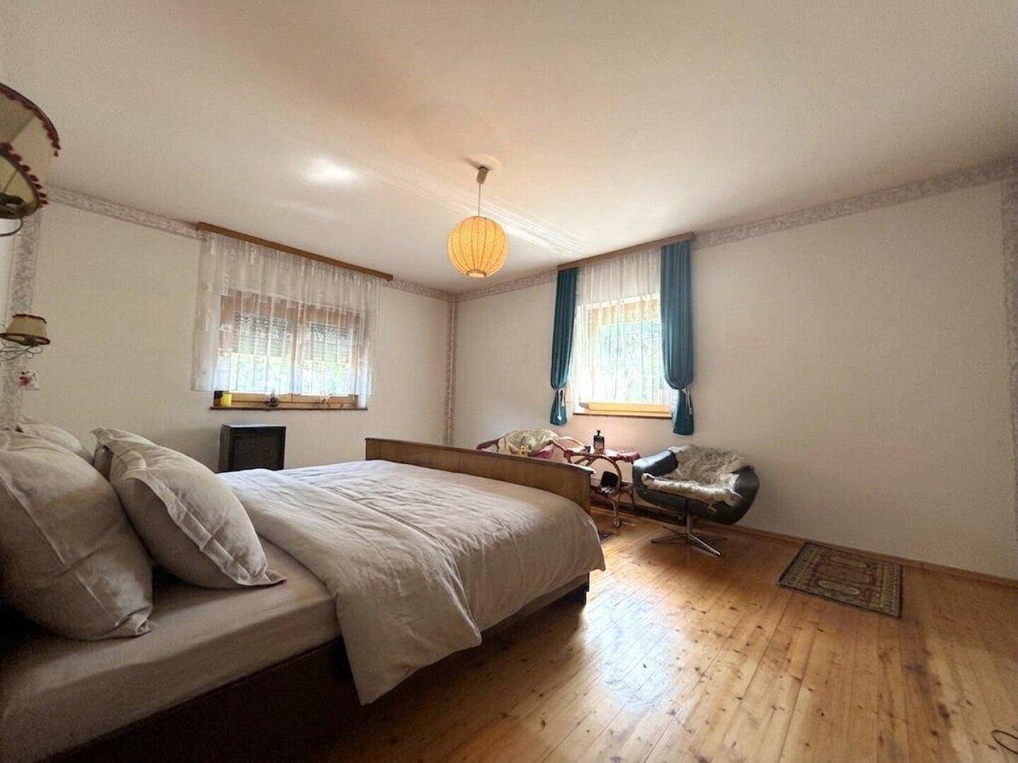 Geräumiges Schlafzimmer mit Holzboden, Doppelbett und zwei Fenstern.