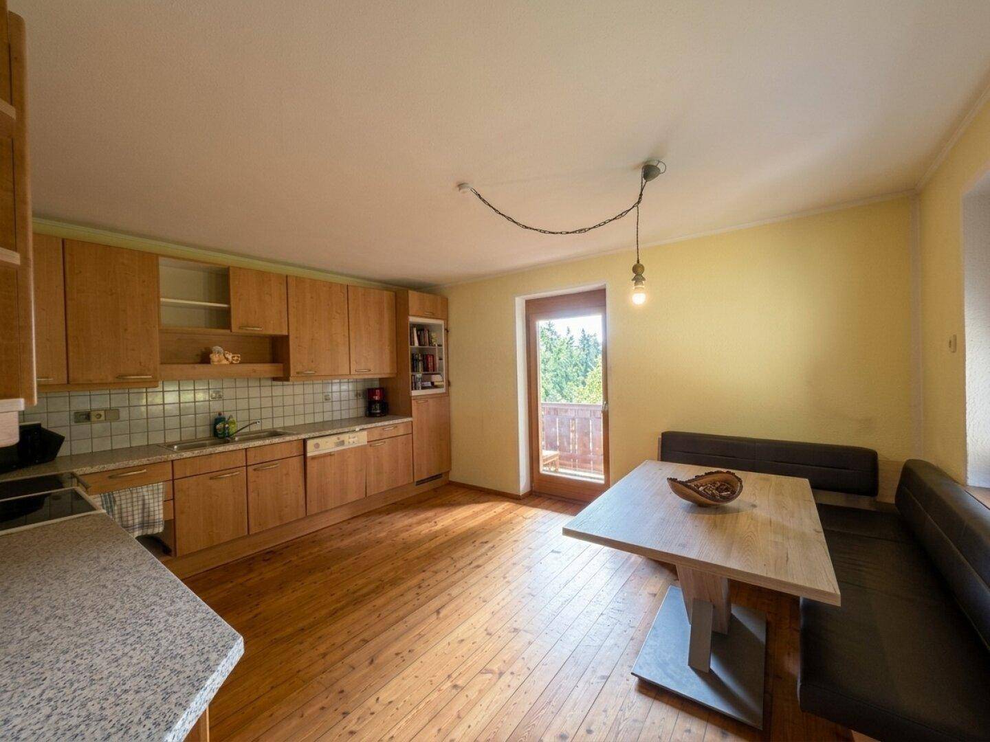 Helle Küche mit Holzboden, Einbauküche und Zugang zu einem Balkon.