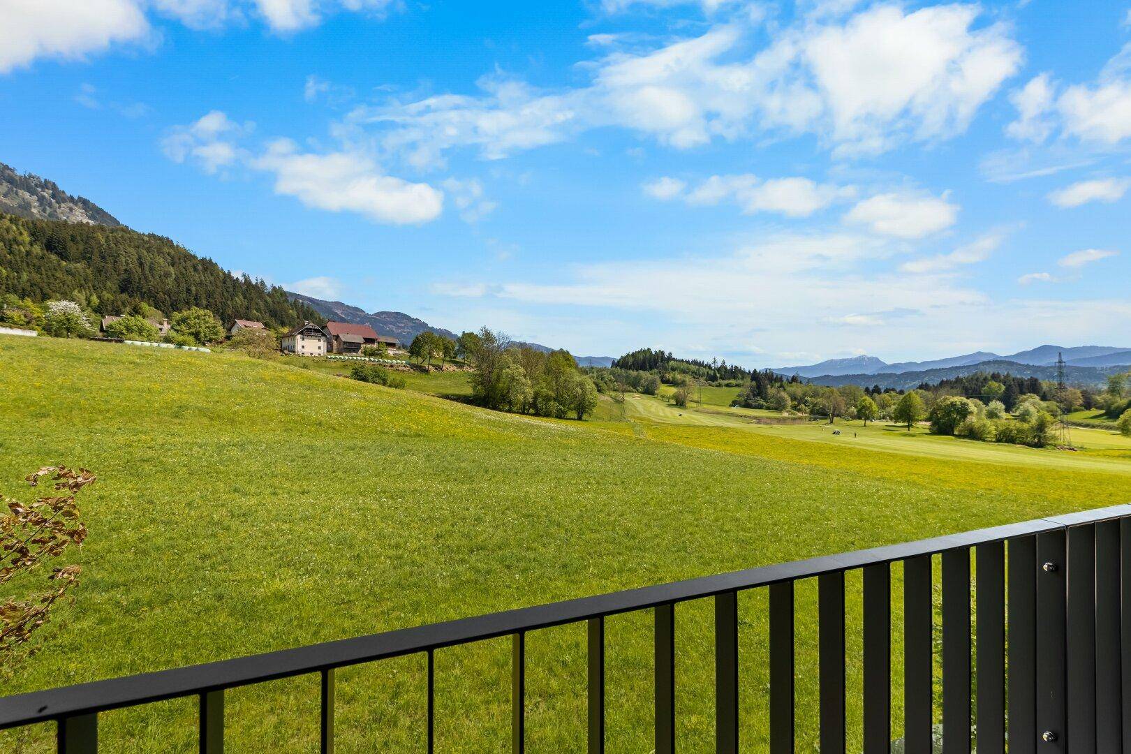 Weitläufiger Blick über grüne Felder und Hügel von einem Balkon oder einer Terrasse.