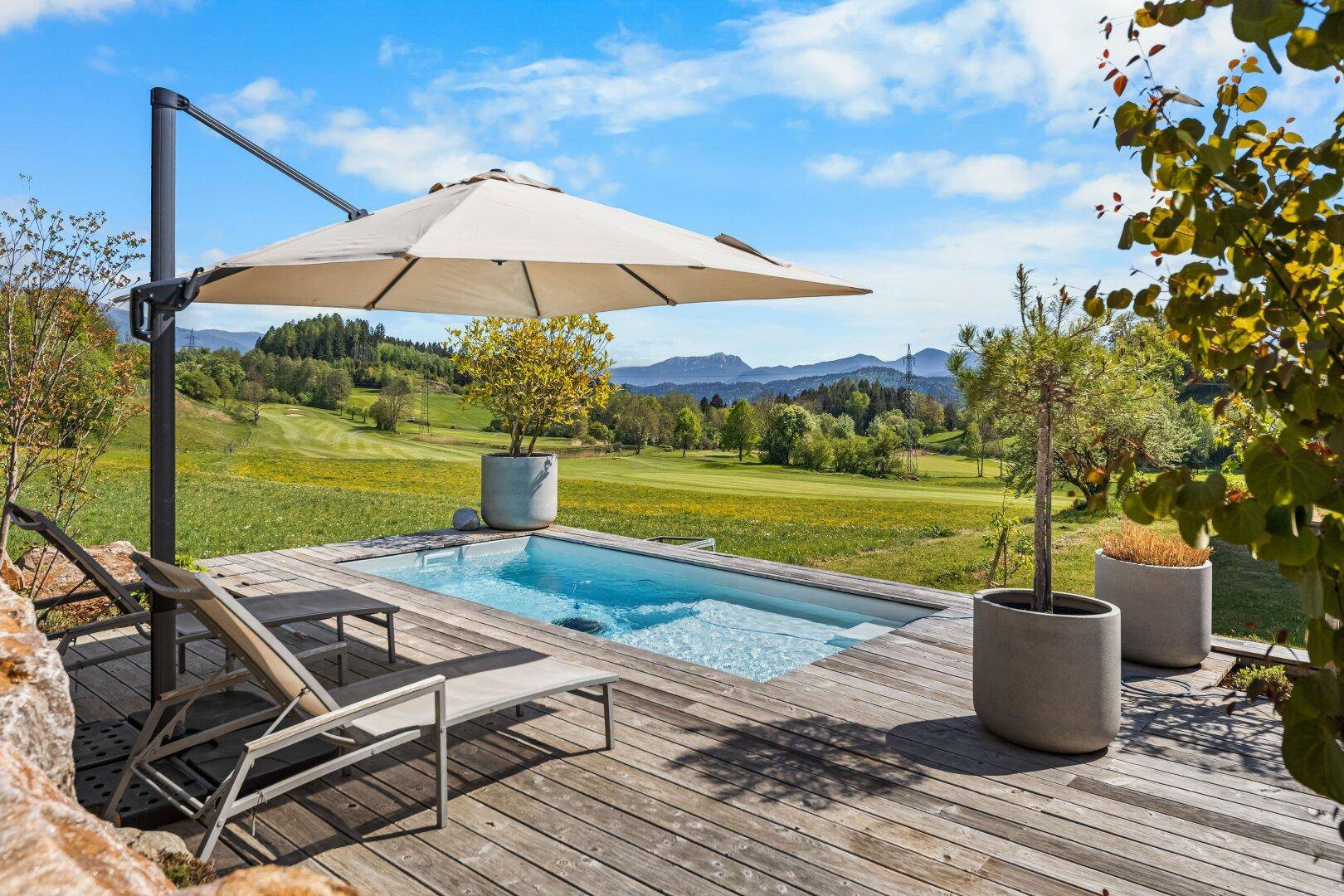 Kleiner Pool auf einer Holzterrasse mit Liegestühlen und weitem Blick ins Grüne.