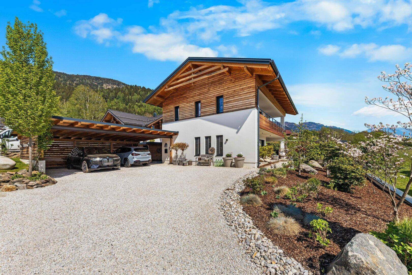 Modernes Einfamilienhaus mit Holzfassade, Carport und gepflegtem Vorgarten.
