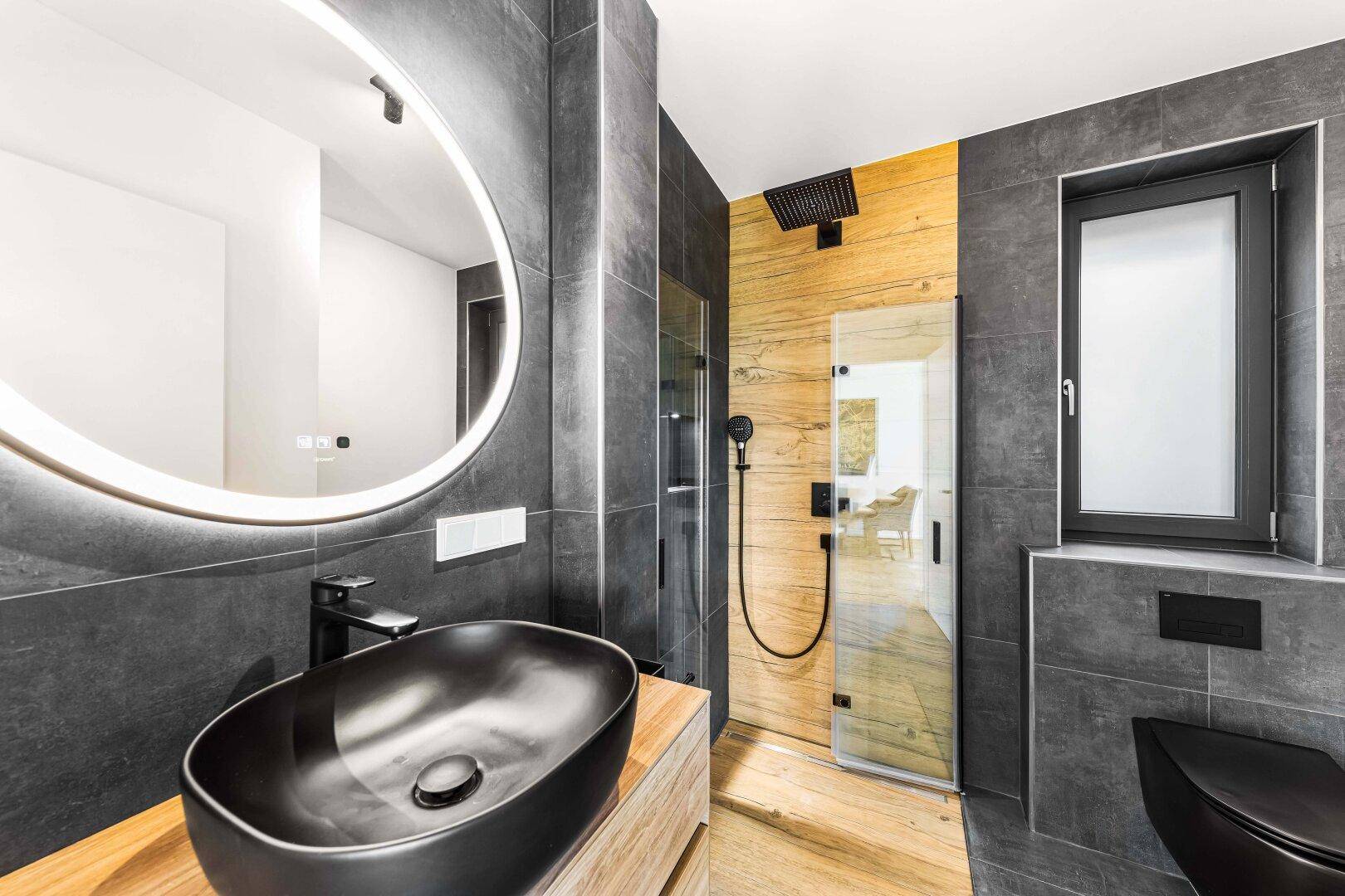 Elegantes Badezimmer mit schwarzem Aufsatzwaschbecken, beleuchtetem Spiegel und moderner Dusche.