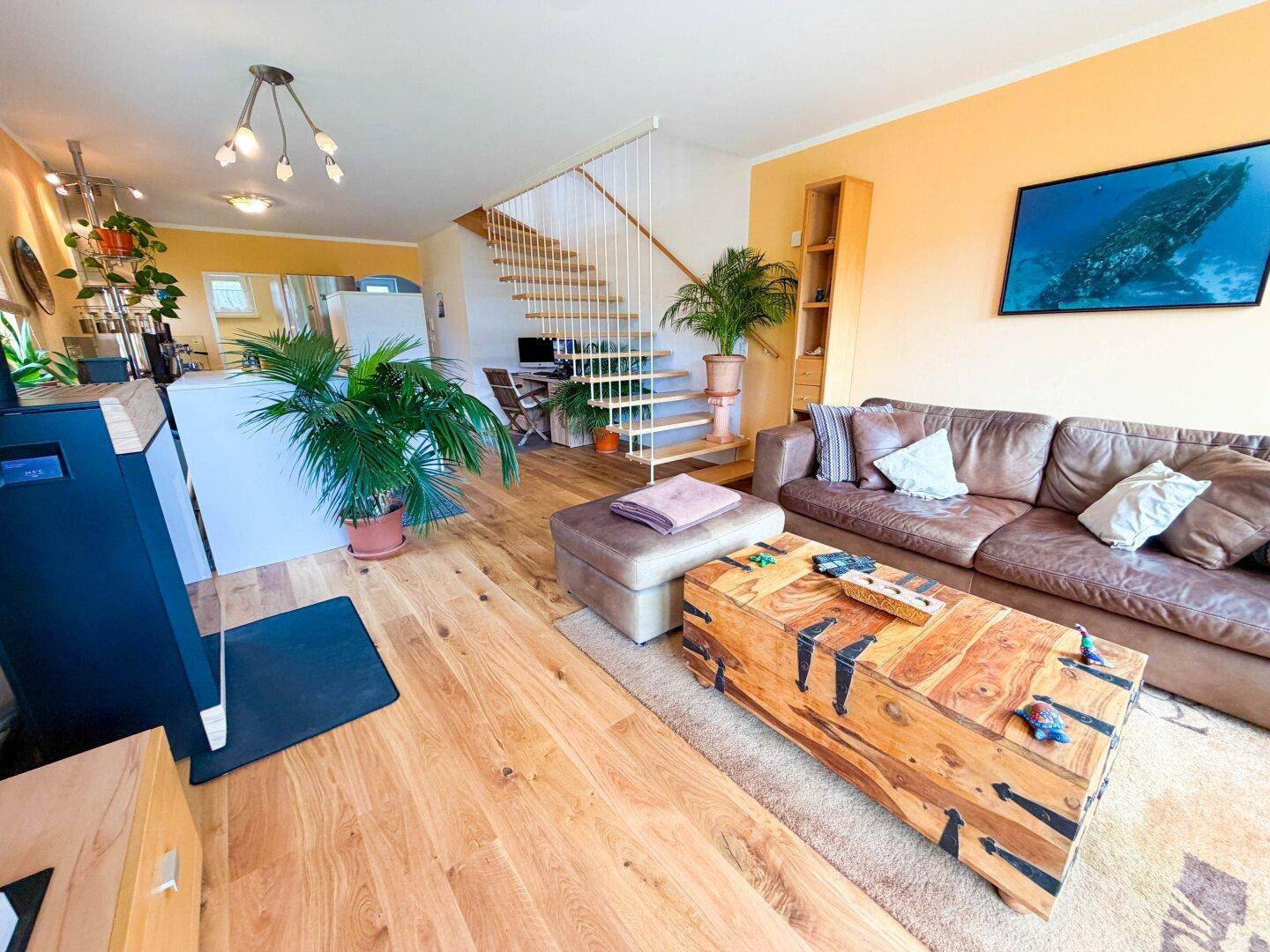 Offener Wohnbereich mit Ledersofa, Holzfußboden und Treppe zum Obergeschoss.