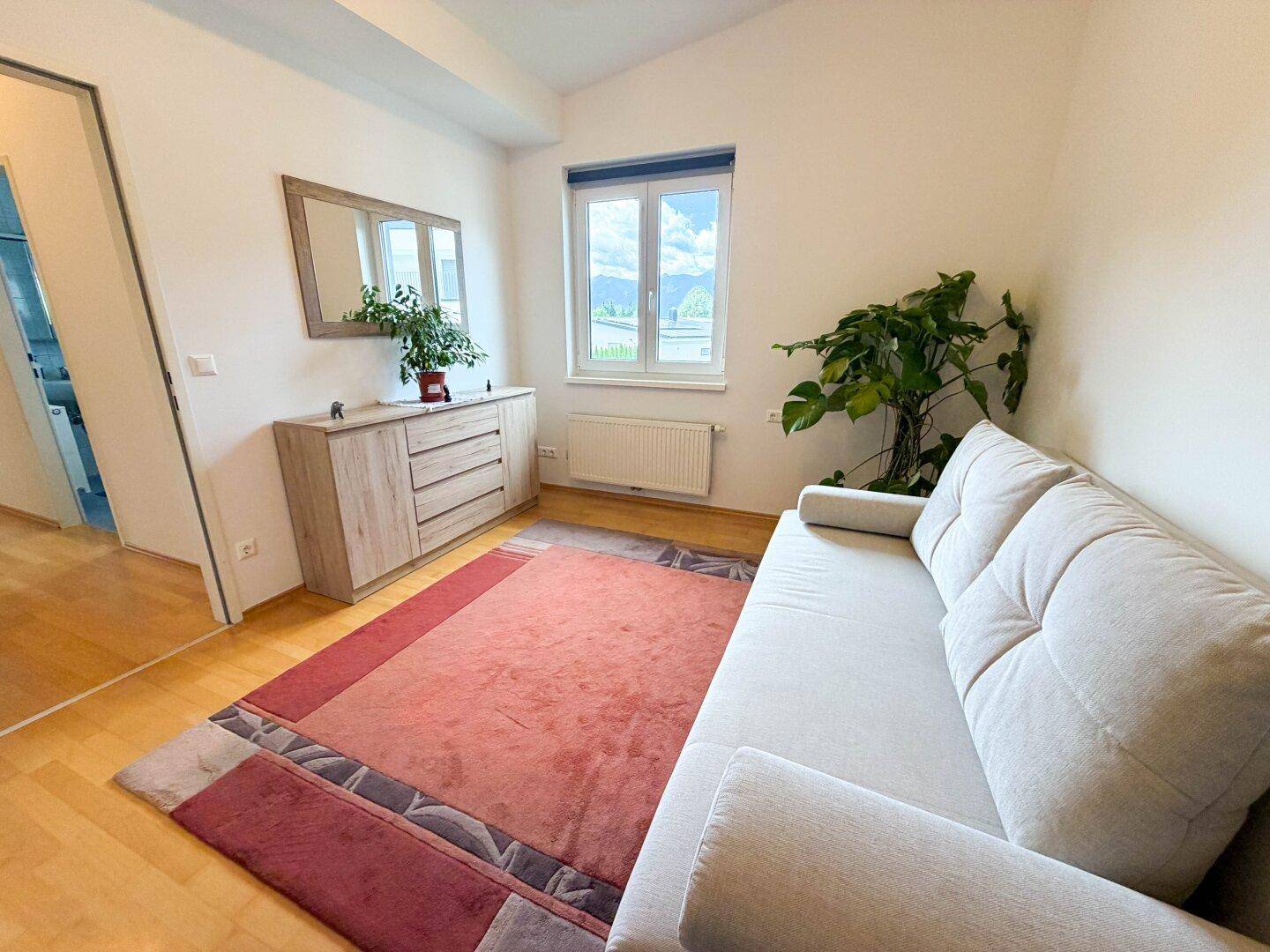 Helles Zimmer mit Sofa, Kommode und Fenster, ideal als Gästezimmer oder Büro.