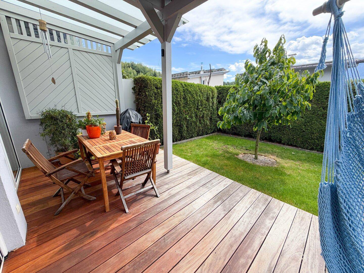 Gemütliche Holzterrasse mit Esstisch, Stühlen und Hängematte im Grünen.