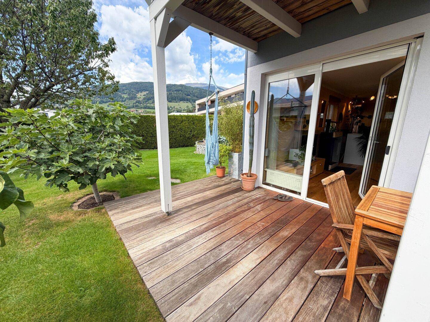 Helle Holzterrasse mit Zugang zum Innenbereich und Blick auf die umliegende Natur.