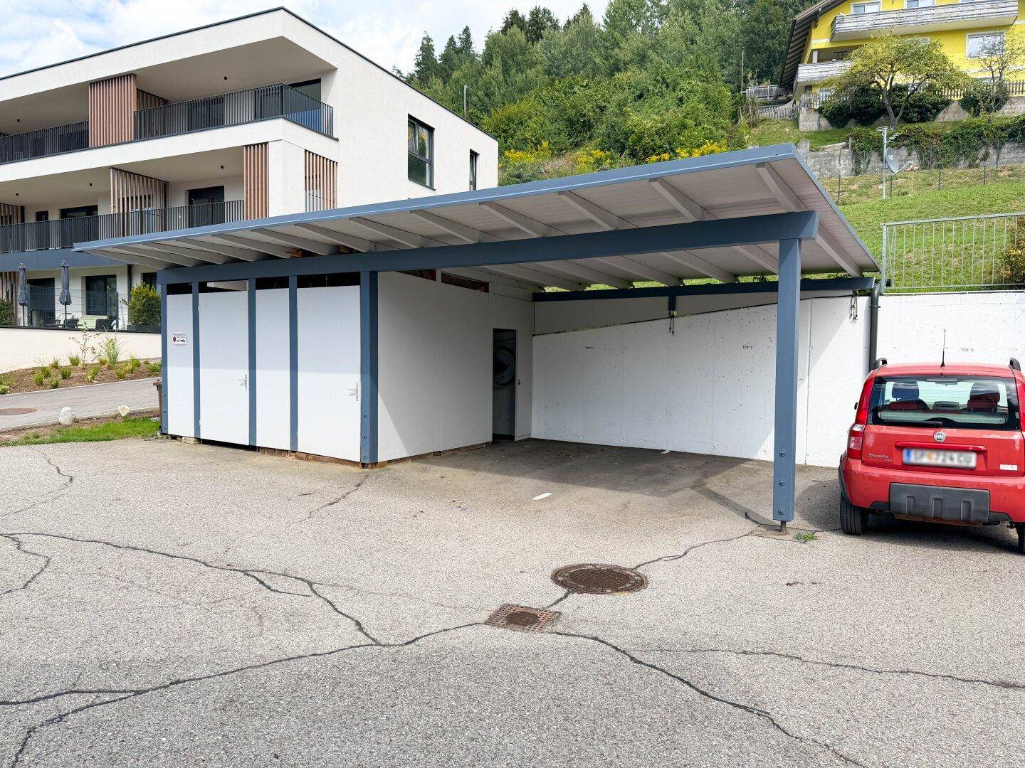 Überdachter Carport-Bereich mit Stellplatz für Fahrzeuge und Abstellräumen.