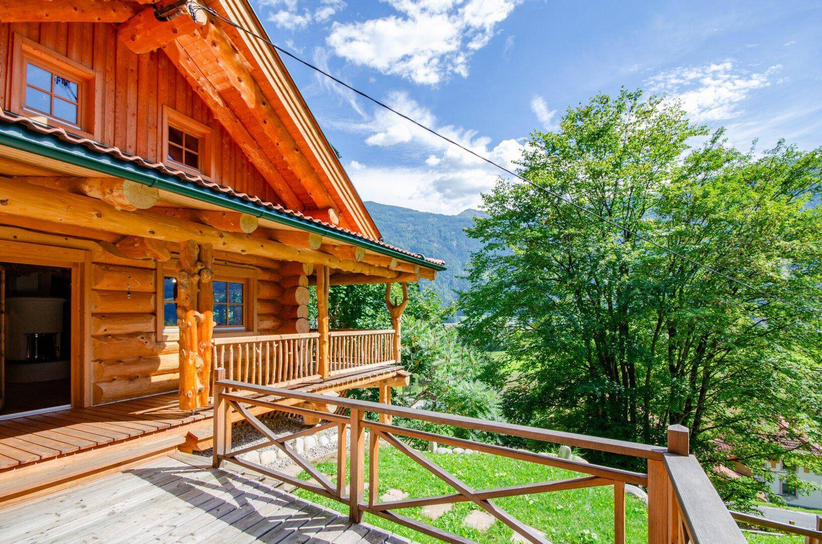 Detailansicht des Holzhauses mit einem sonnigen Balkon und Blick auf die umliegende Berglandschaft.