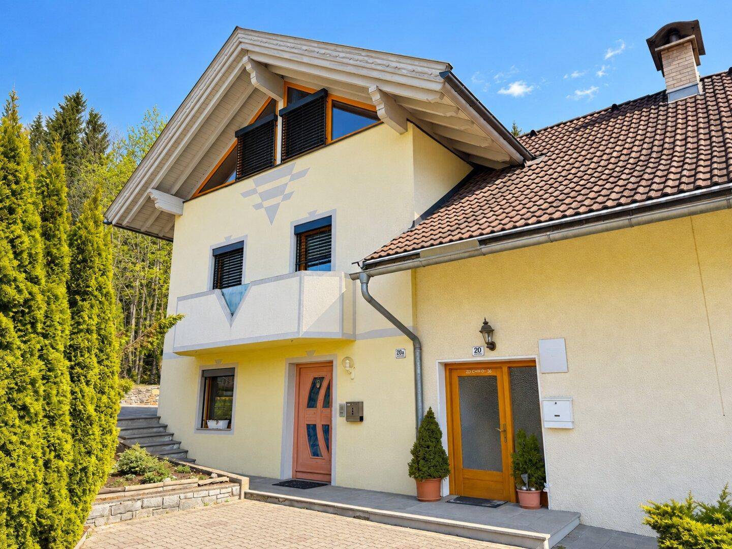 Vorderansicht des Hauses mit zwei Eingängen, Balkon und grünen Hecken.