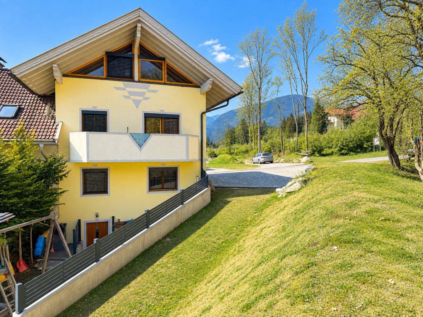 Gelbes Haus mit Gartenbereich, Spielplatz und weitem Blick auf die umliegende Landschaft.