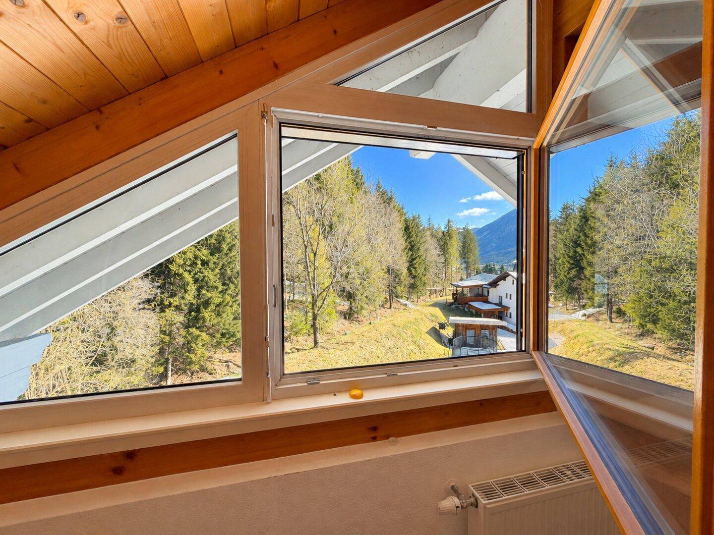 Dachzimmer mit Holzdecke und großen Fenstern, die einen weiten Blick ins Grüne bieten.