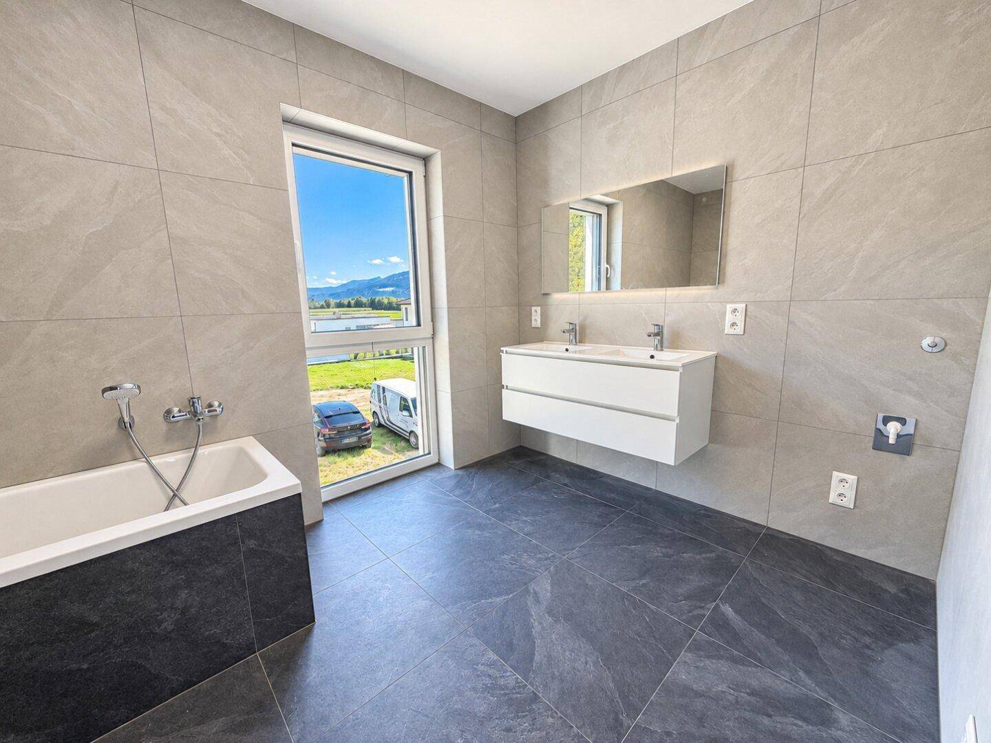 Modernes Badezimmer mit Badewanne, Doppelwaschbecken und großem Fenster.