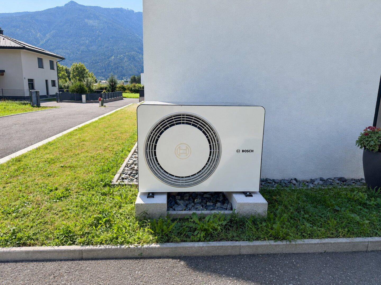 Moderne Wärmepumpe von Bosch an der Hauswand in grüner Umgebung.