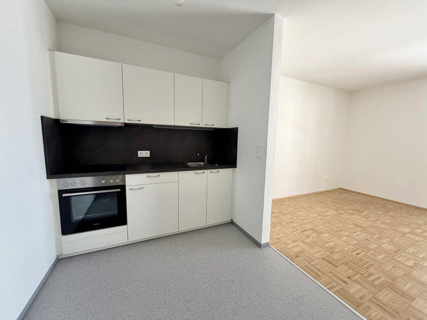 Funktionale Küchenzeile mit weißen Schränken, schwarzer Arbeitsplatte und integriertem Backofen.
