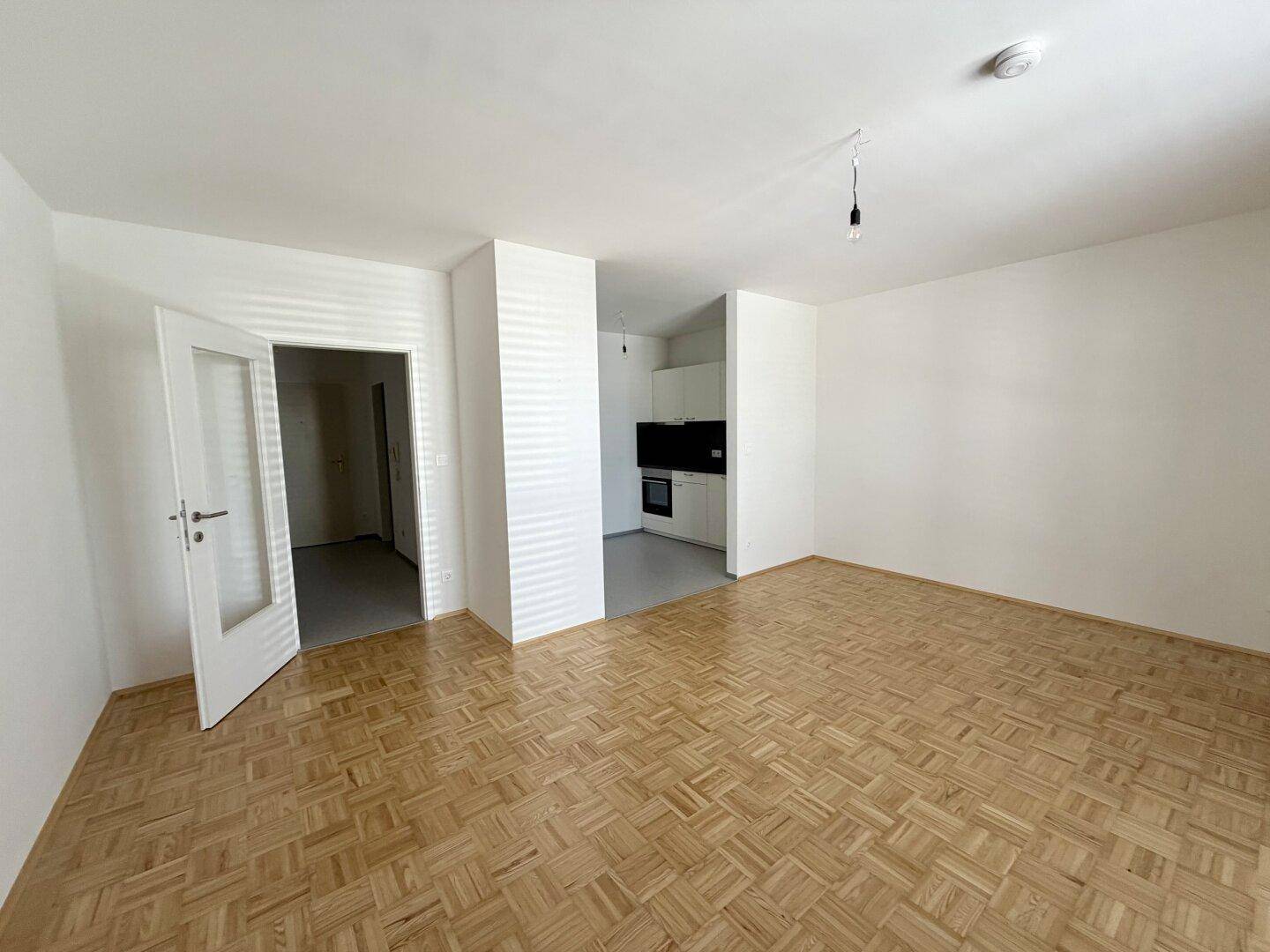 Geräumiger Wohnbereich mit Parkettboden und Zugang zu einem angrenzenden Küchenbereich.