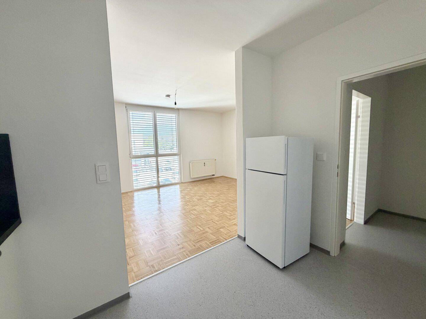 Eingangsbereich mit Kühlschrank und Blick in den Wohnbereich sowie ein weiteres Zimmer.