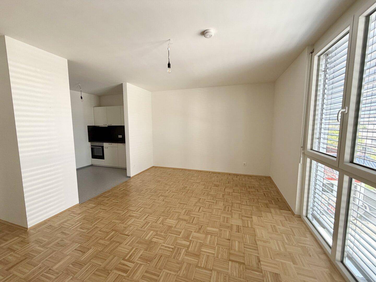 Heller Wohnraum mit Parkettboden und großem Fenster, das einen Blick nach draußen bietet.