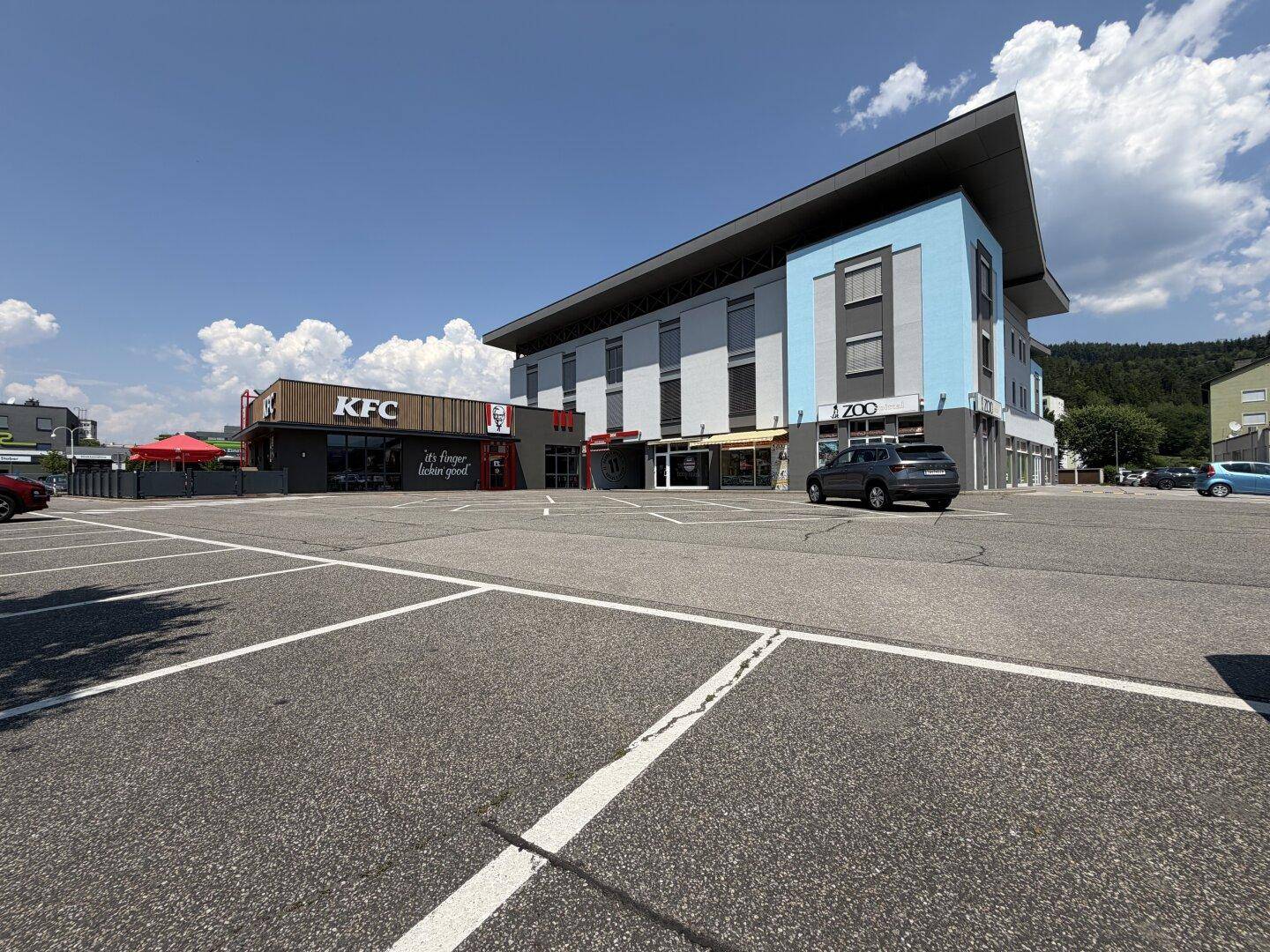 Außenansicht eines modernen Gebäudes mit angrenzendem Parkplatz und Gewerbeflächen.