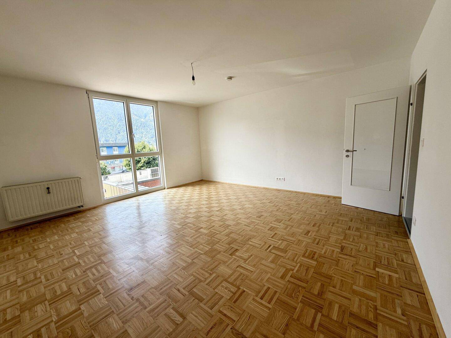 Geräumiges Wohnzimmer mit Parkettboden, großen Fenstern und viel Tageslicht.
