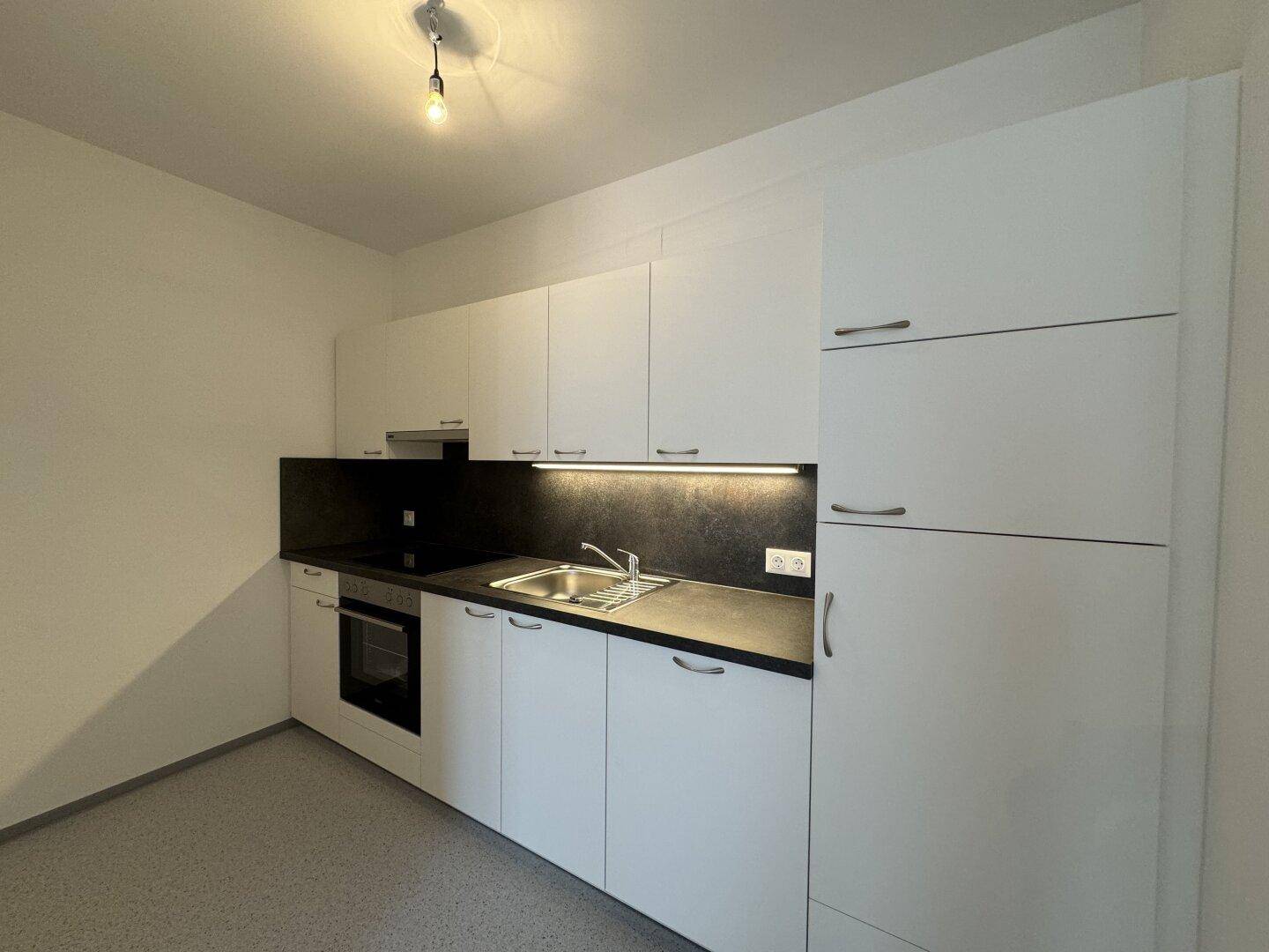 Moderne Einbauküche mit weißen Schränken, dunkler Arbeitsplatte und integrierten Geräten.