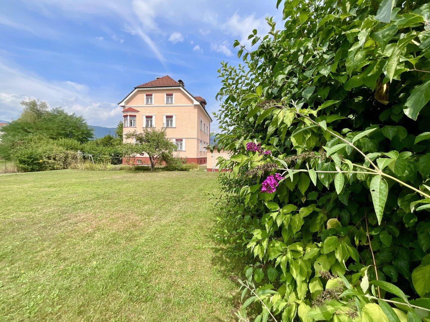 Großer Gartenbereich mit üppigem Grün und dem historischen Gebäude im Hintergrund.
