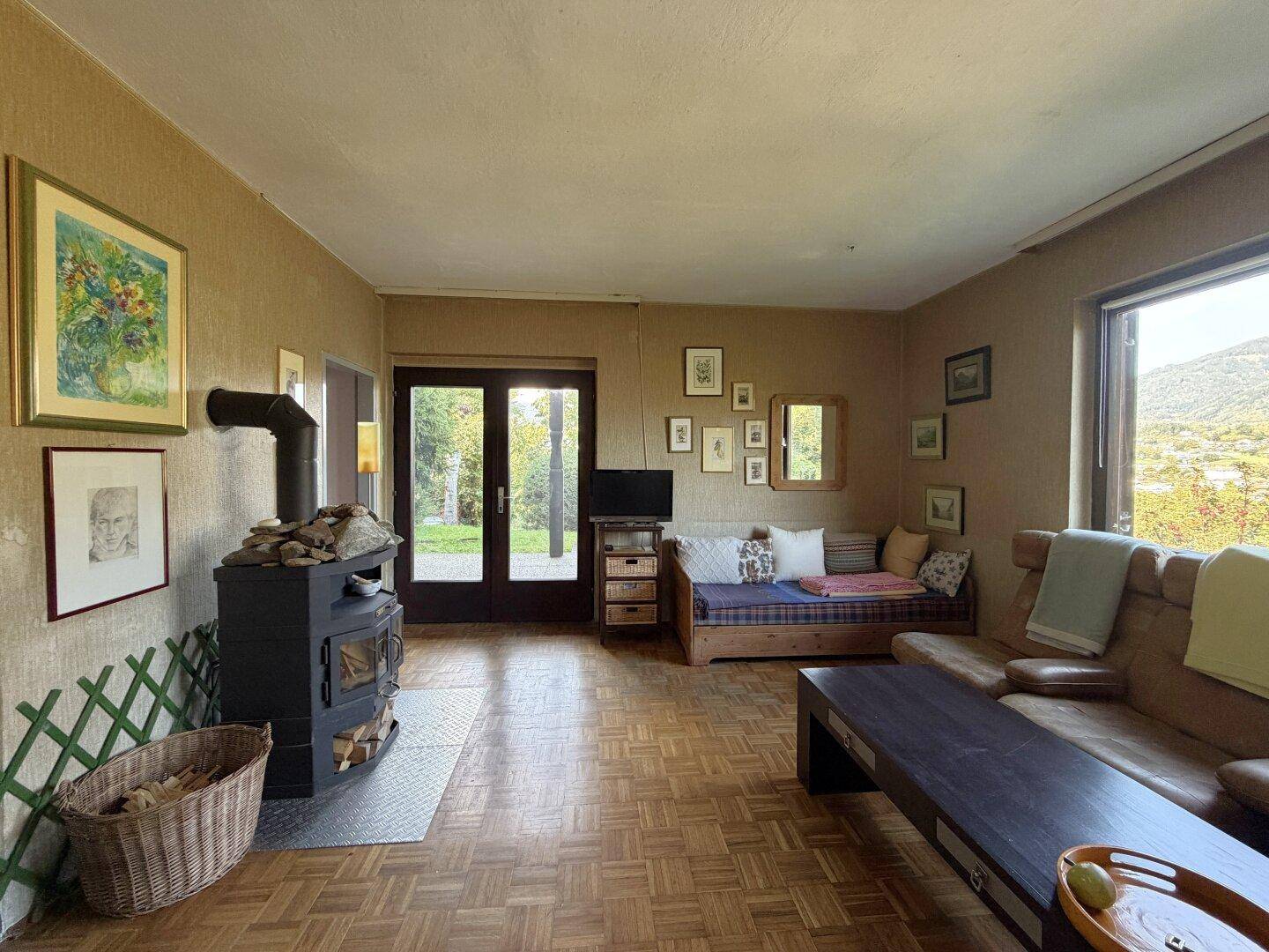 Gemütliches Wohnzimmer mit Holzofen, Parkettboden und Zugang zum Garten.