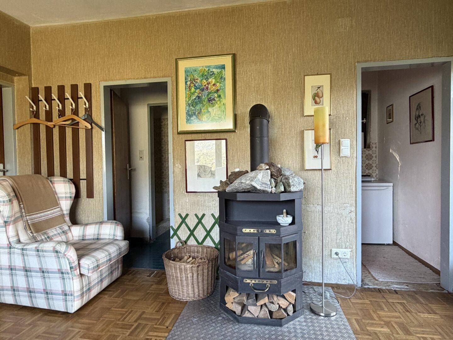 Rustikaler Holzofen als Mittelpunkt des Wohnzimmers mit kariertem Sessel und Holzboden.