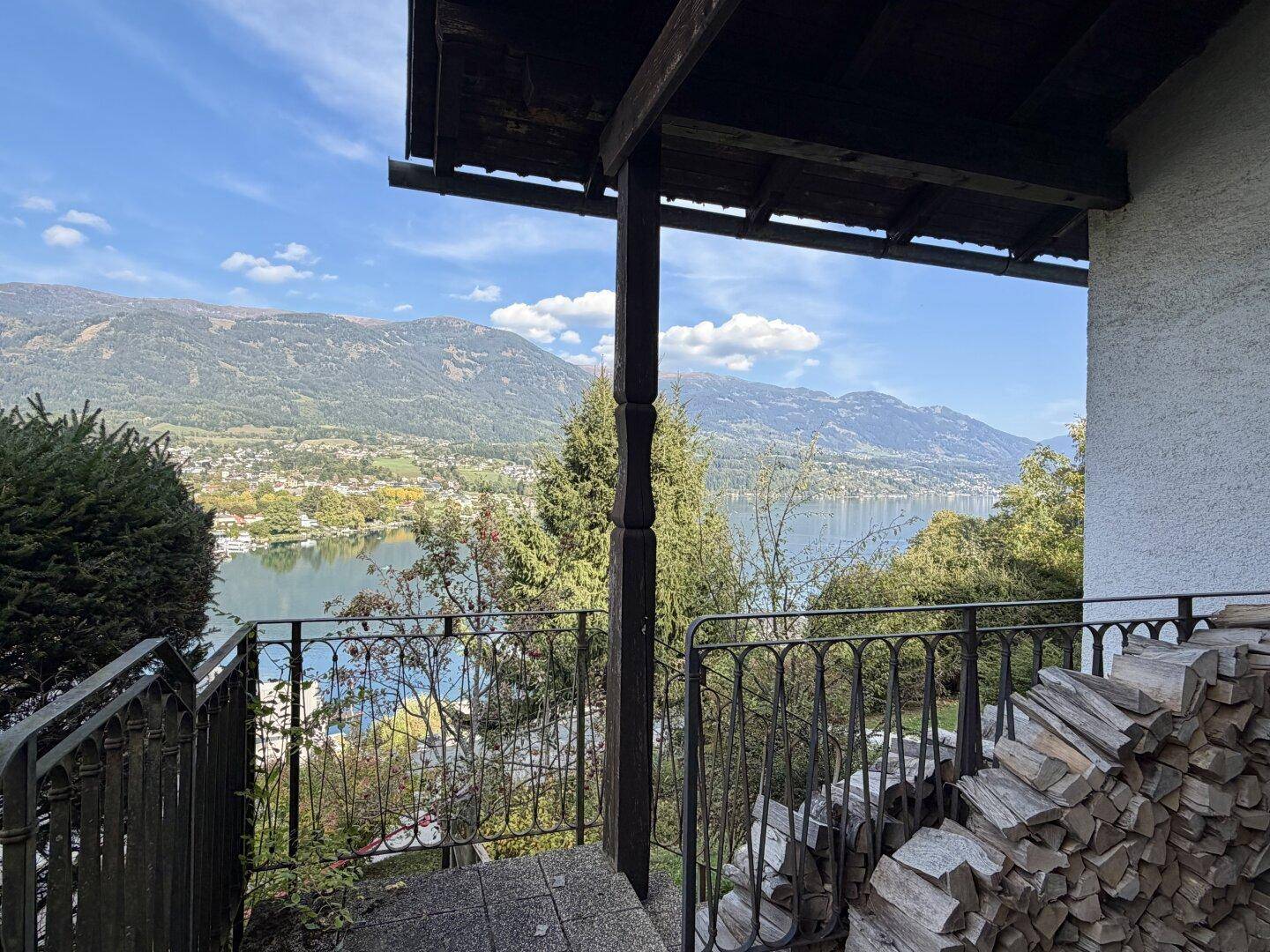 Überdachter Balkon mit Seeblick, Holzstapel und schmiedeeisernem Geländer.