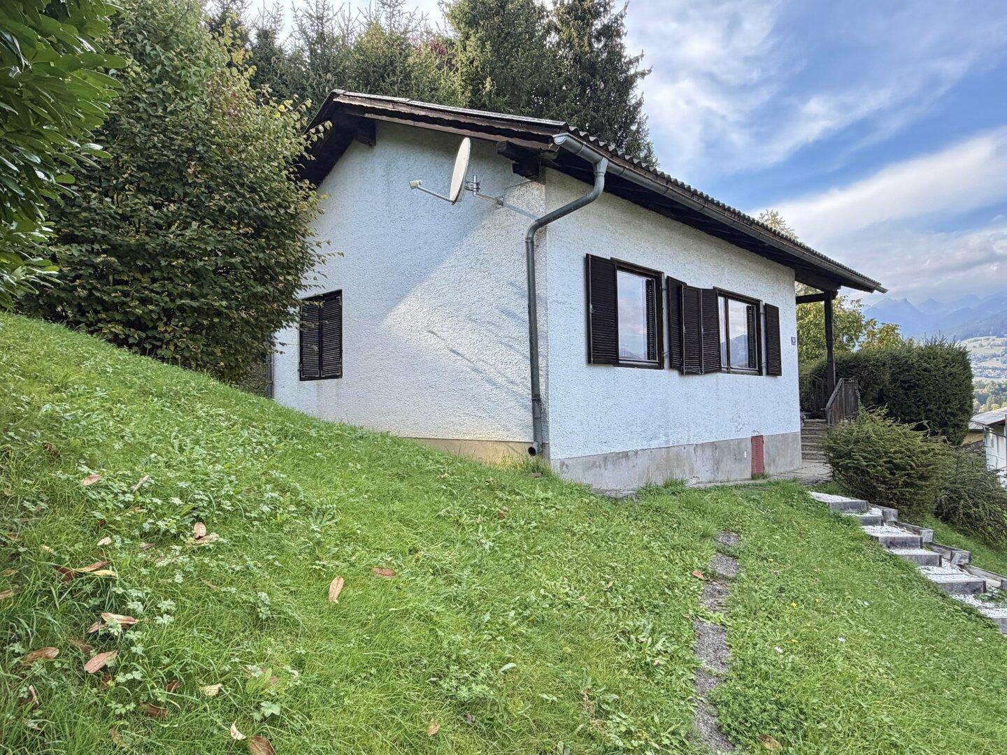 Seitenansicht eines Hauses mit weißer Fassade, grüner Wiese und Satellitenschüssel.