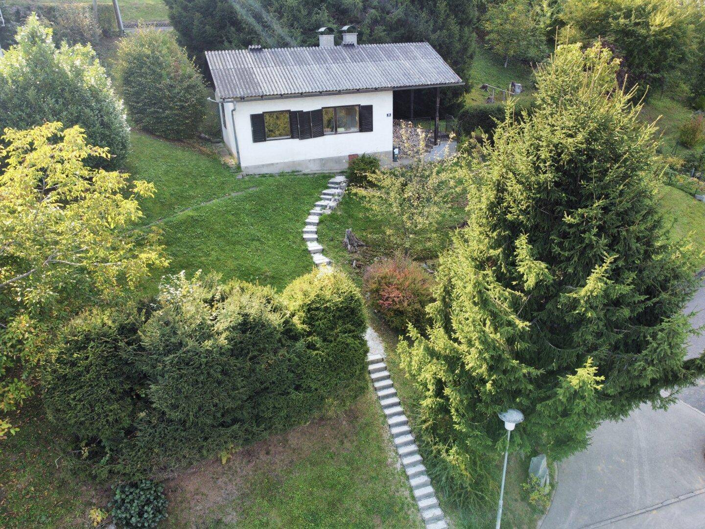 Luftaufnahme eines charmanten Hauses mit Garten und Steinpfad in grüner Umgebung.