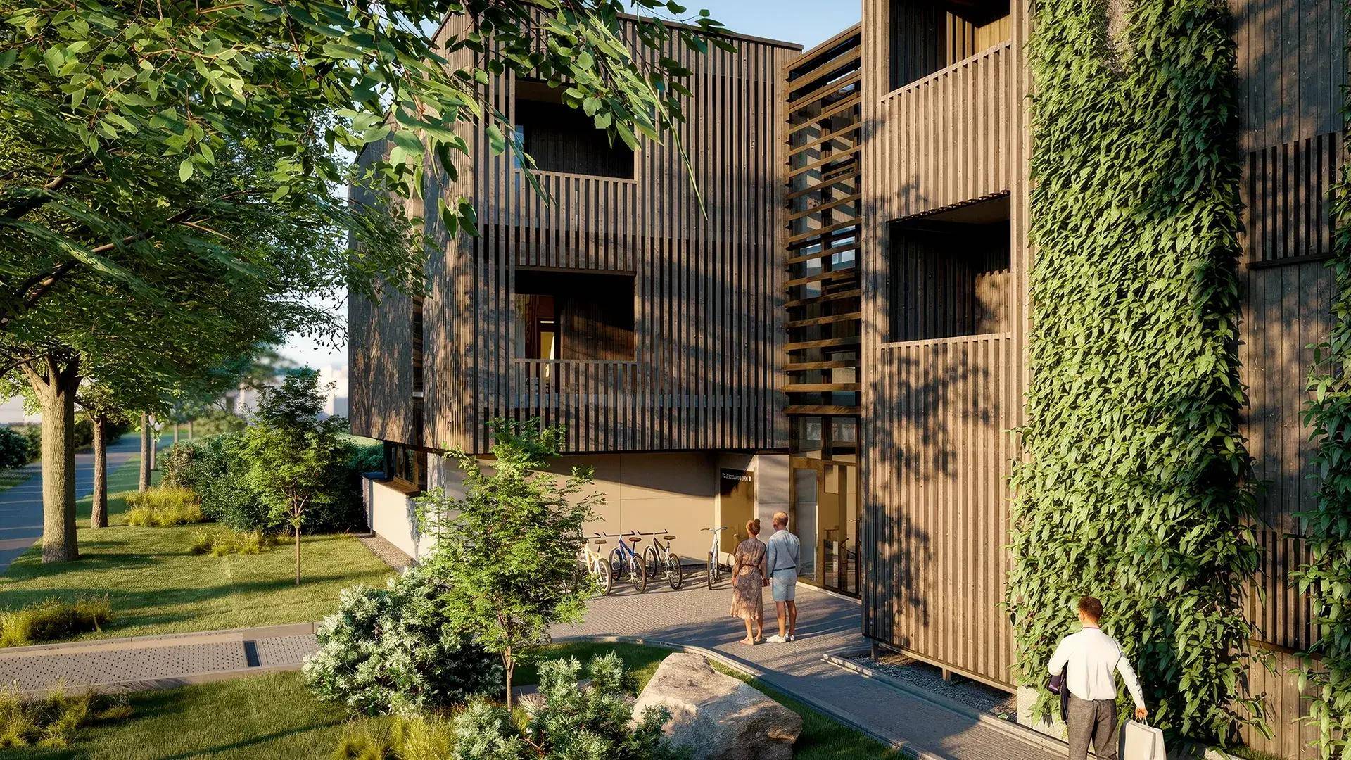 Eingangsbereich eines modernen Gebäudes mit vertikalen Holzlamellen, üppigem Grün und Fußweg.