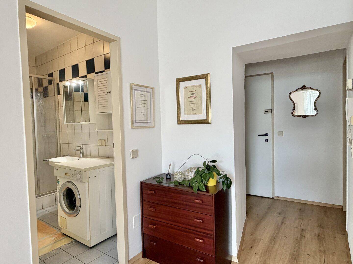 Eingangsbereich mit Kommode und Blick in das geflieste Badezimmer mit Waschmaschine.