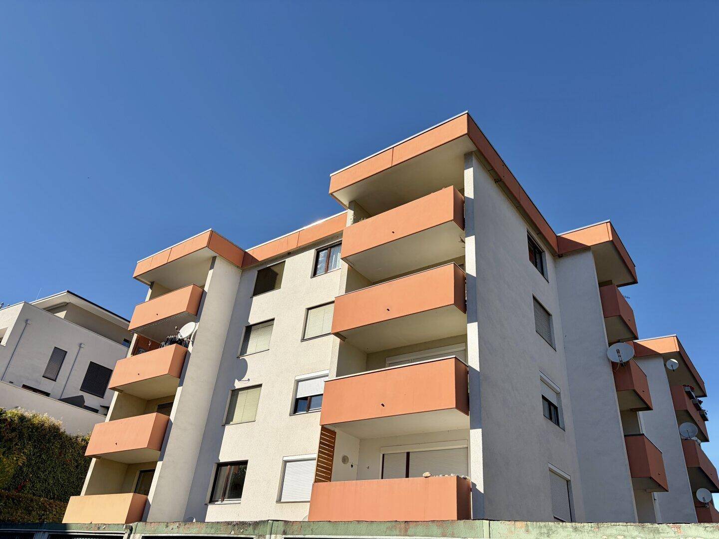 Mehrstöckiges Wohngebäude mit zahlreichen Balkonen unter blauem Himmel.