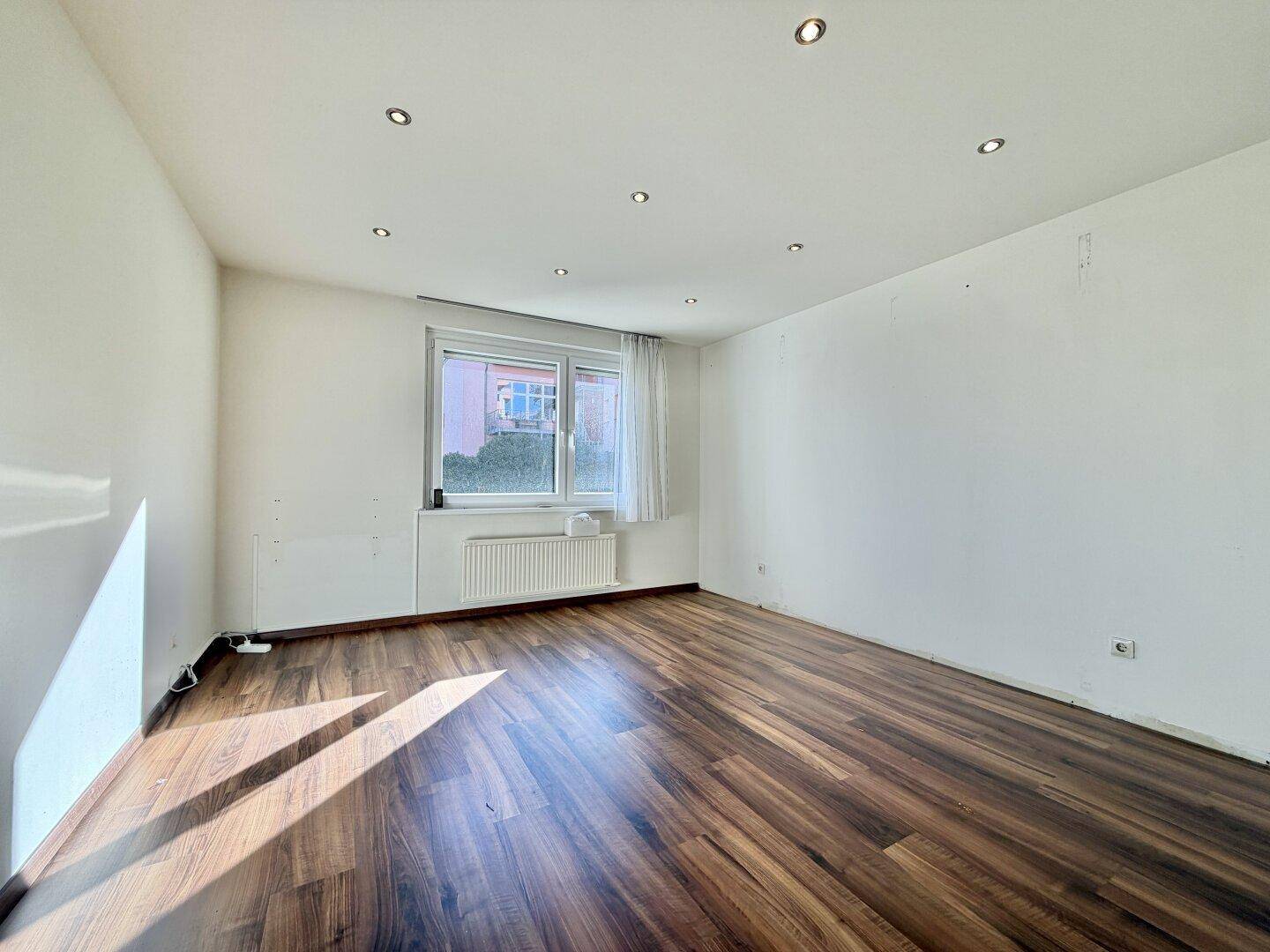 Heller Raum mit dunklem Laminatboden und Einbaustrahlern in der Decke.
