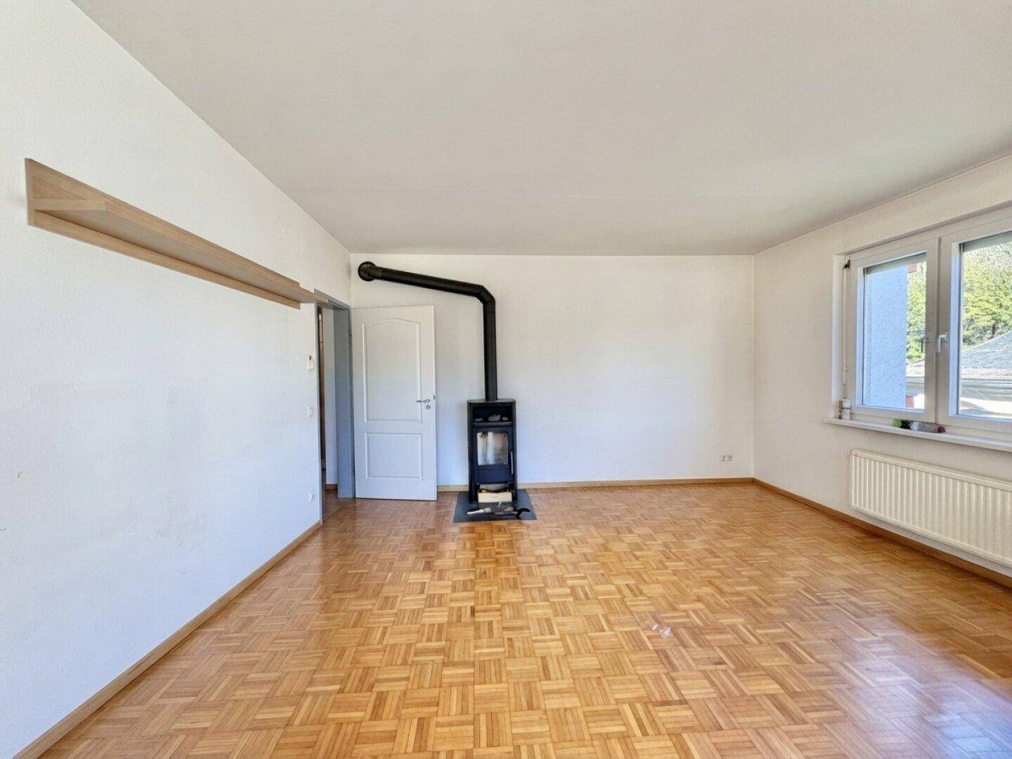 Geräumiges Wohnzimmer mit Parkettboden und einem modernen Holzofen als Heizquelle.