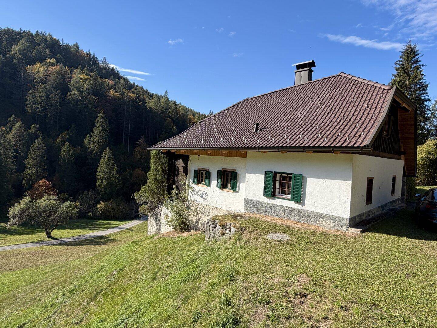 Traditionelles Haus mit weißer Fassade, grünen Fensterläden und braunem Ziegeldach.