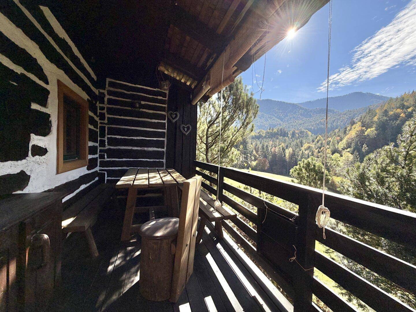 Sonniger Holzbalkon mit rustikalen Möbeln und weitem Blick auf die umliegenden Berge.
