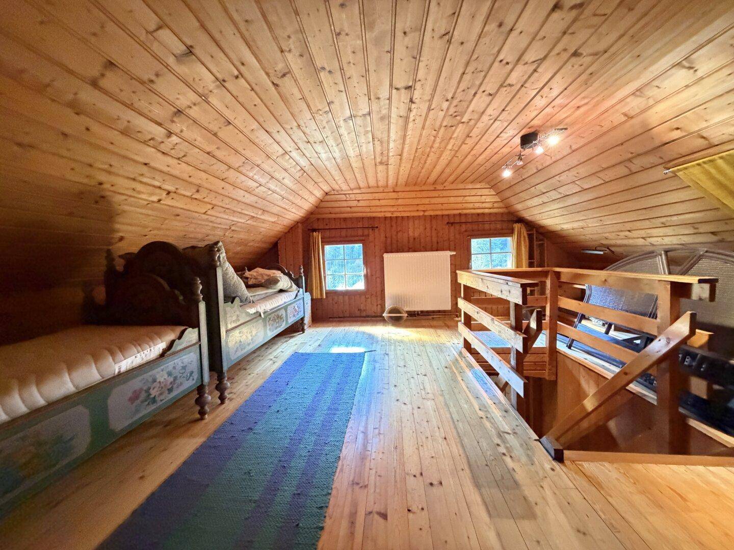 Geräumiger Dachboden mit Holzboden, Dachschrägen und zwei Einzelbetten.