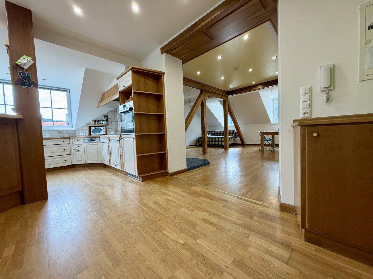 Offener Wohnbereich mit integrierter Küche, Holzbalken und Parkettboden, ideal für geselliges Beisammensein.