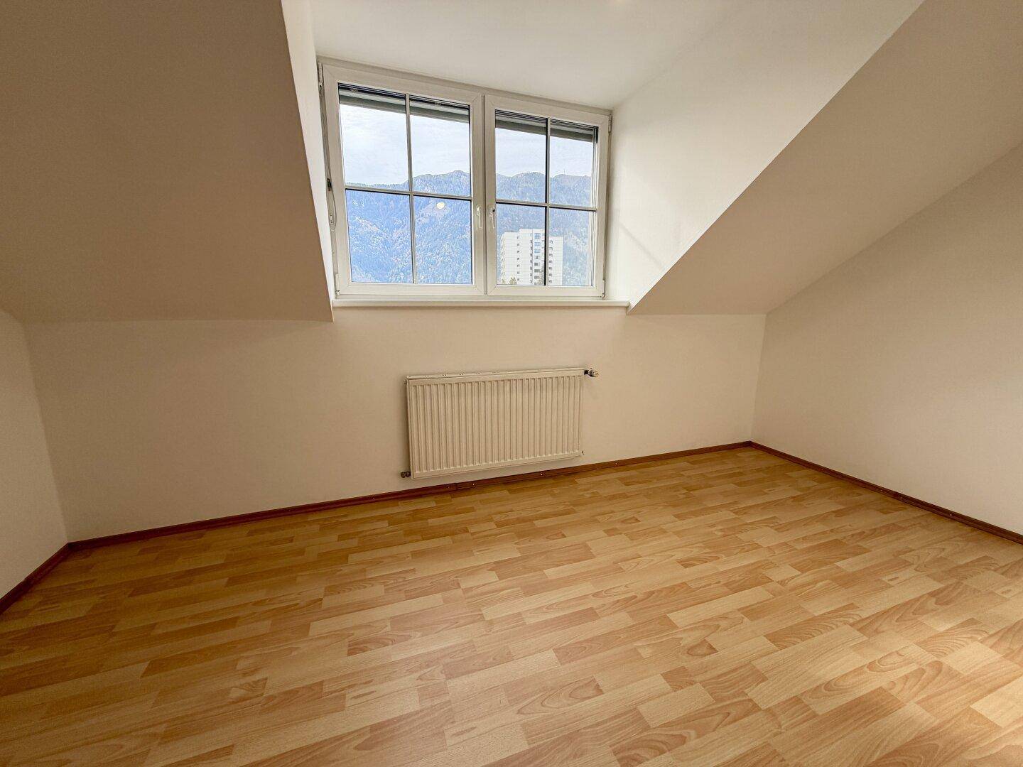 Helles Schlafzimmer mit Laminatboden, Dachschräge und Fenster mit Blick auf die Berge.