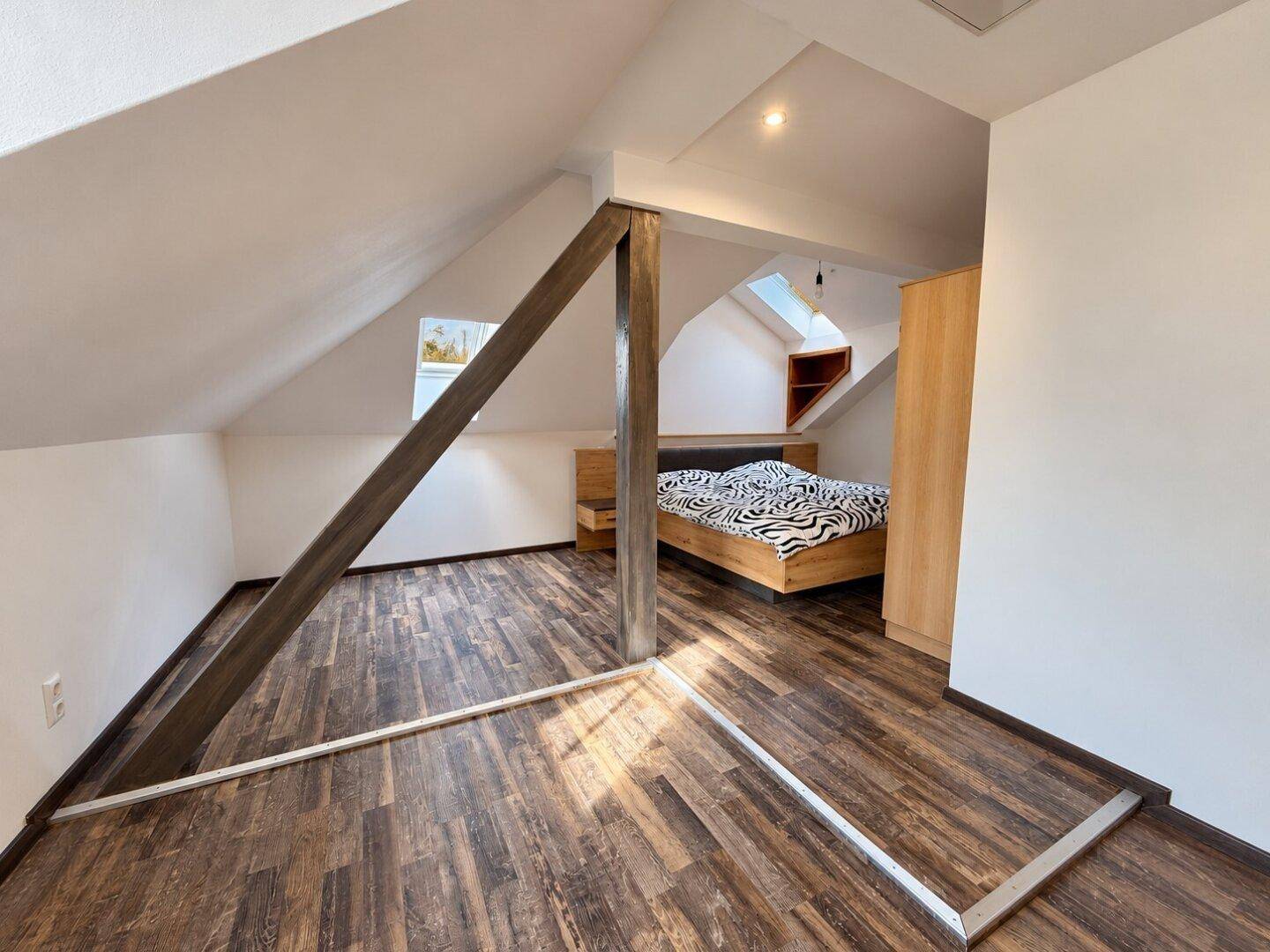 Schlafzimmer unter der Dachschräge mit Holzbett, Laminatboden und Dachfenstern für natürliches Licht.