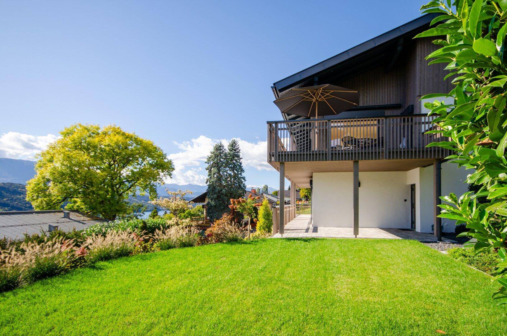 Gepflegter Gartenbereich mit Rasenfläche und Blick auf das Haus mit Balkon und See.