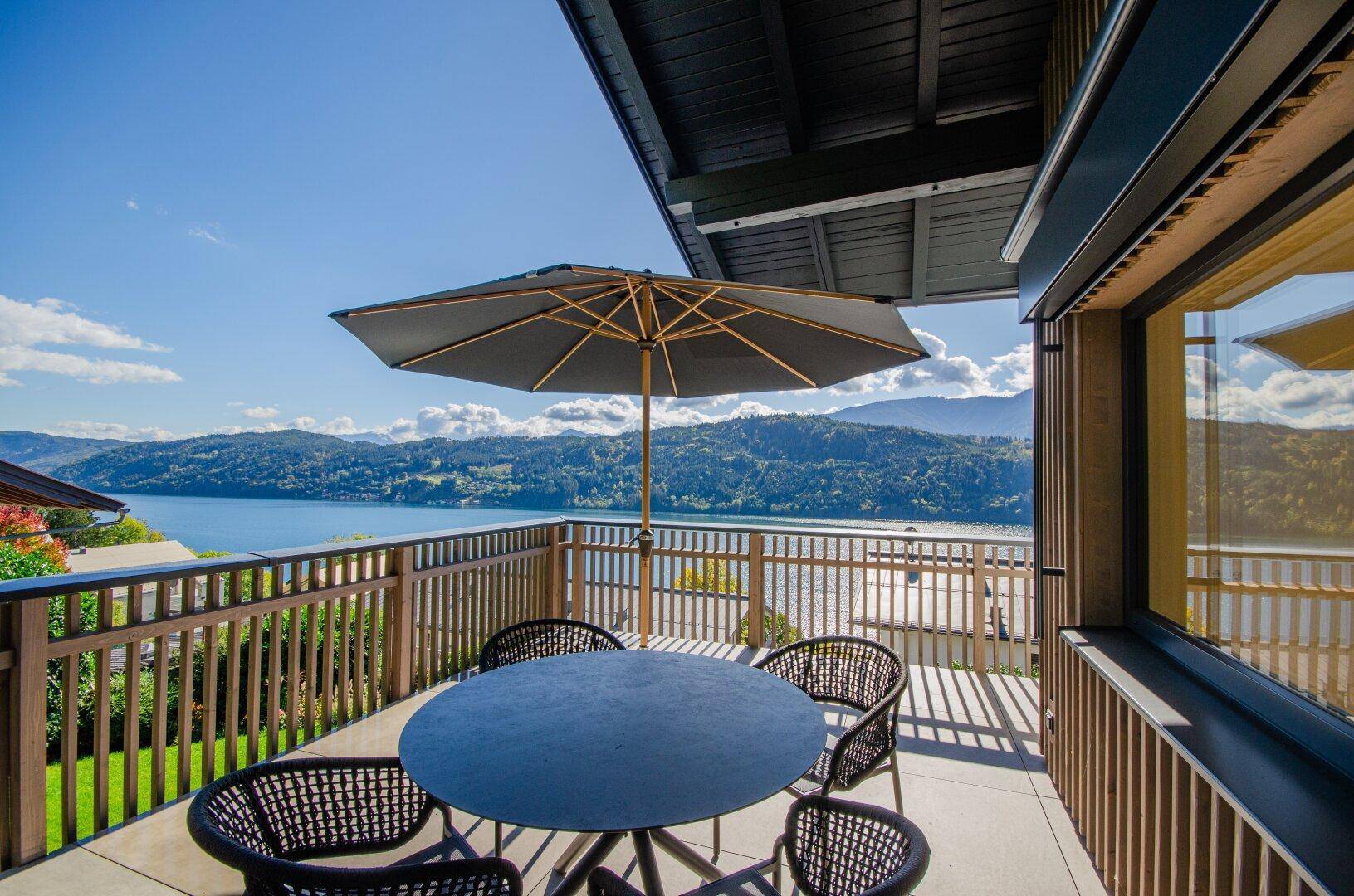 Sonniger Balkon mit Esstisch, Sonnenschirm und weitem Blick über den See und die Berge.