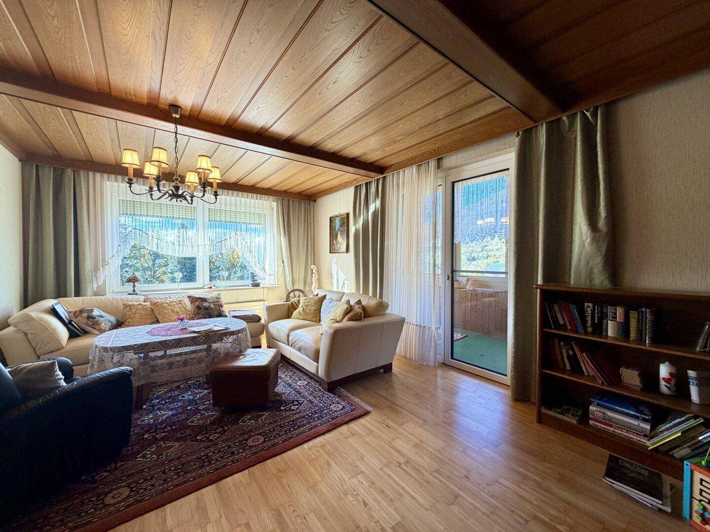Helles Wohnzimmer mit Holzbalkendecke, Parkettboden und direktem Zugang zum Balkon.
