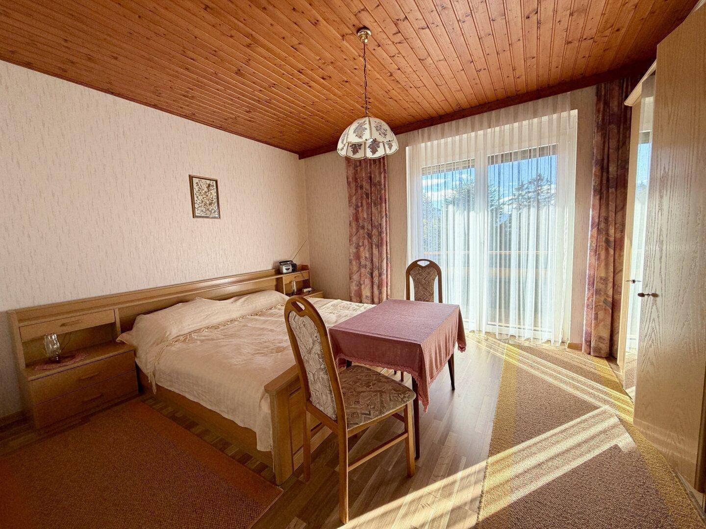 Helles Schlafzimmer mit Holzbalkendecke, Doppelbett und direktem Zugang zum Balkon.