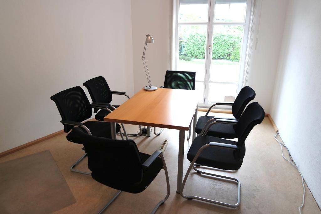 Besprechungsraum mit Holztisch, schwarzen Bürostühlen und großem Fenster mit Blick ins Grüne.