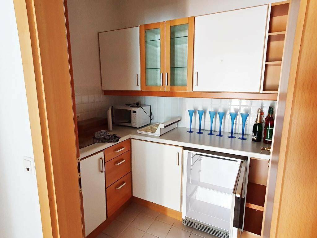 Kleine Küchenzeile mit weißen und holzfarbenen Schränken, Mikrowelle und integriertem Kühlschrank.