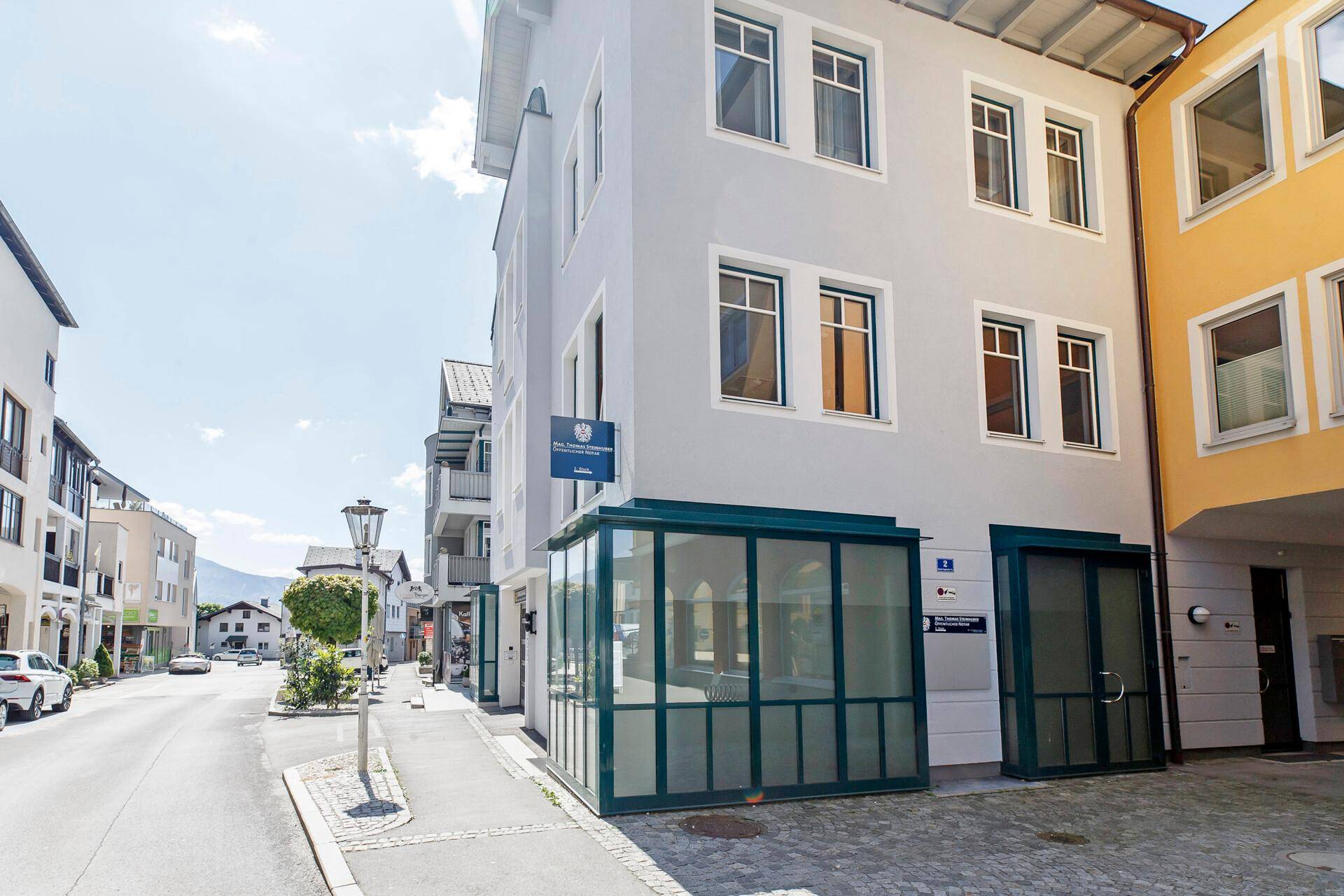 Modernes Geschäftsgebäude an einer belebten Straße mit großen Fenstern und einem gläsernen Eingangsbereich.